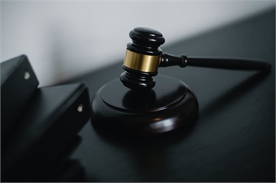 [ai] A close-up of a wooden gavel with a gold band placed on a dark surface, next to black binder files.